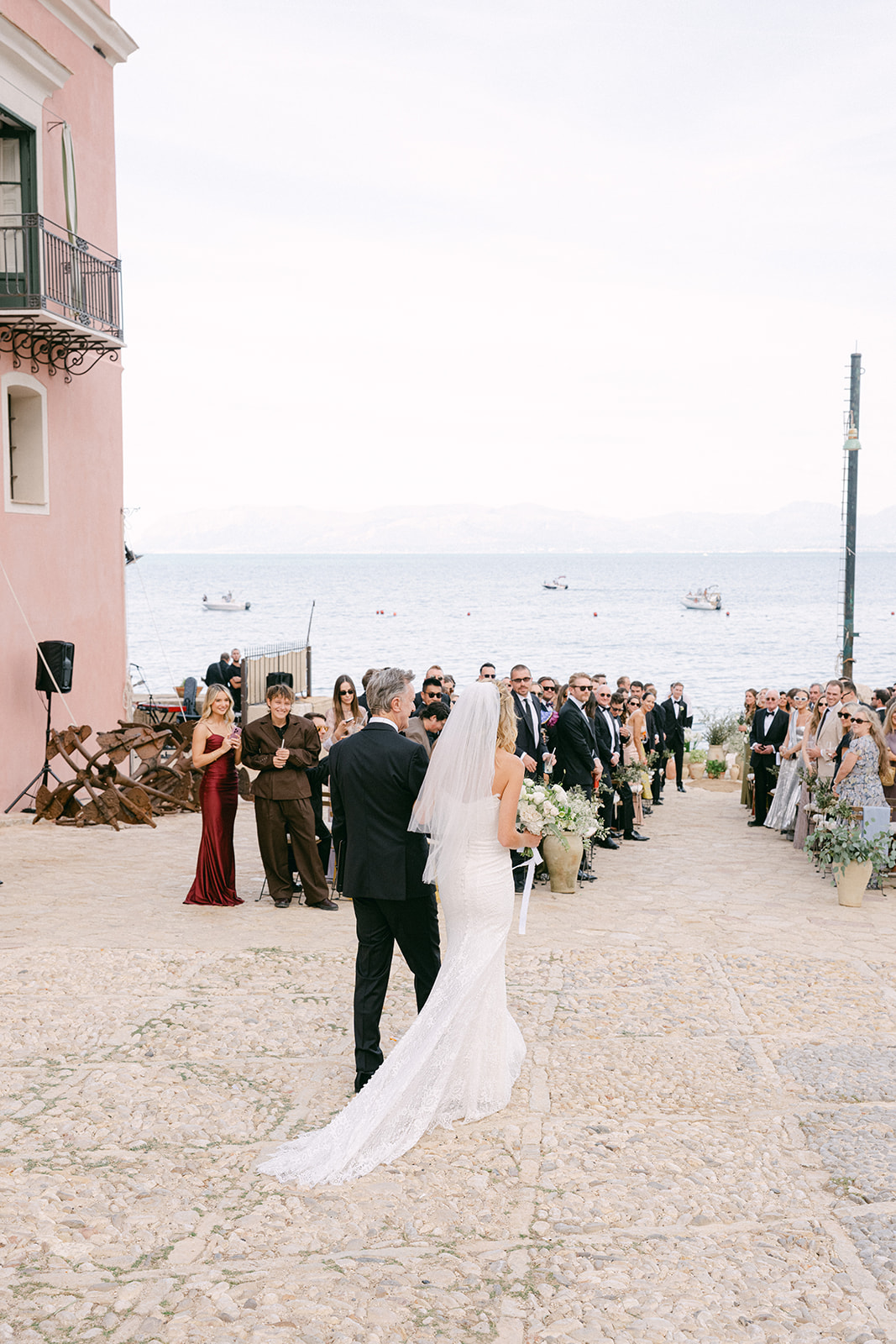bride walking down the aisle with her father for the outdoor wedding ceremony in Tonnara di Scopello