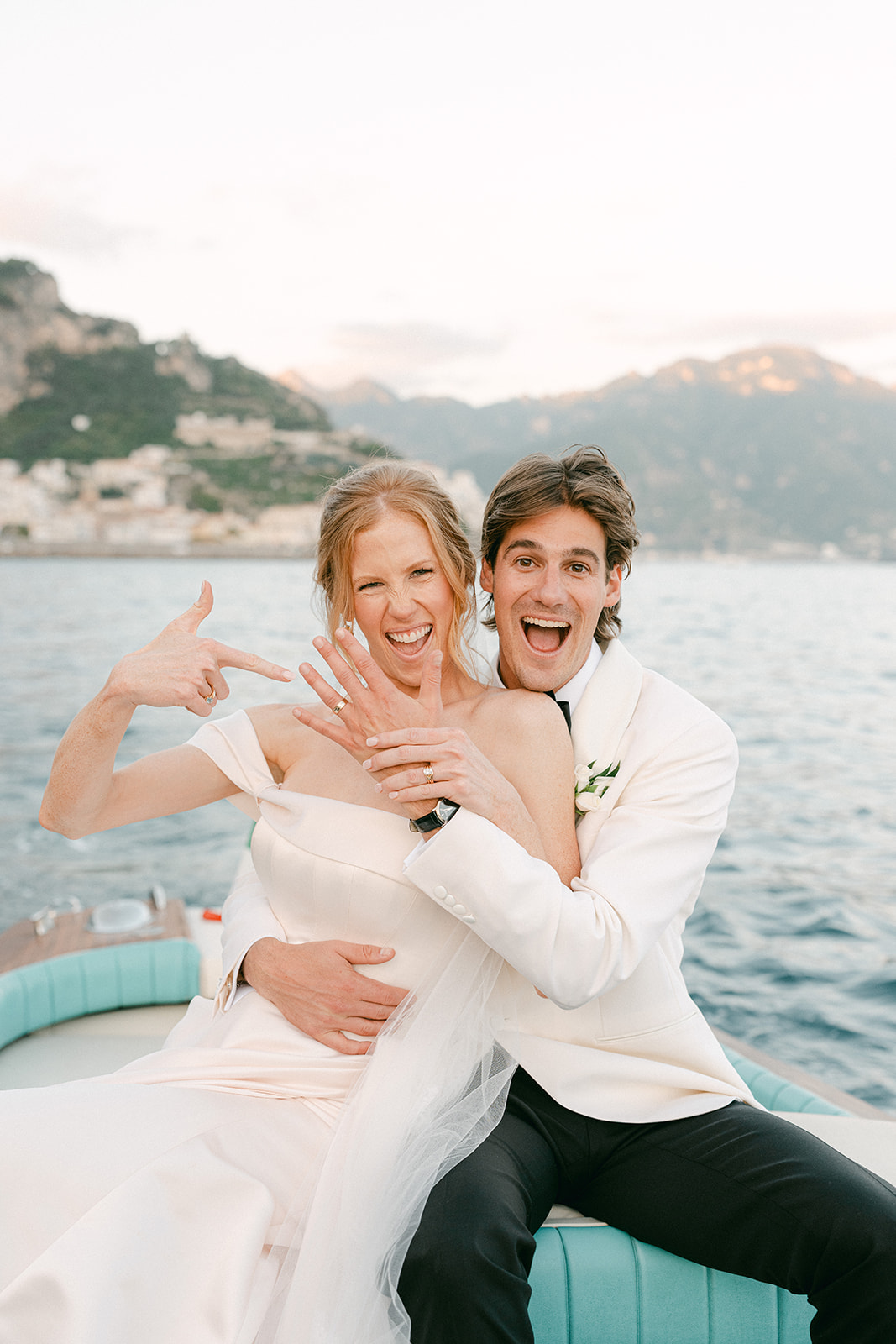 Newly married couple standing on a yacht along the Amalfi Coast, capturing elegant wedding portraits with Mediterranean blue waters and dramatic cliffs.