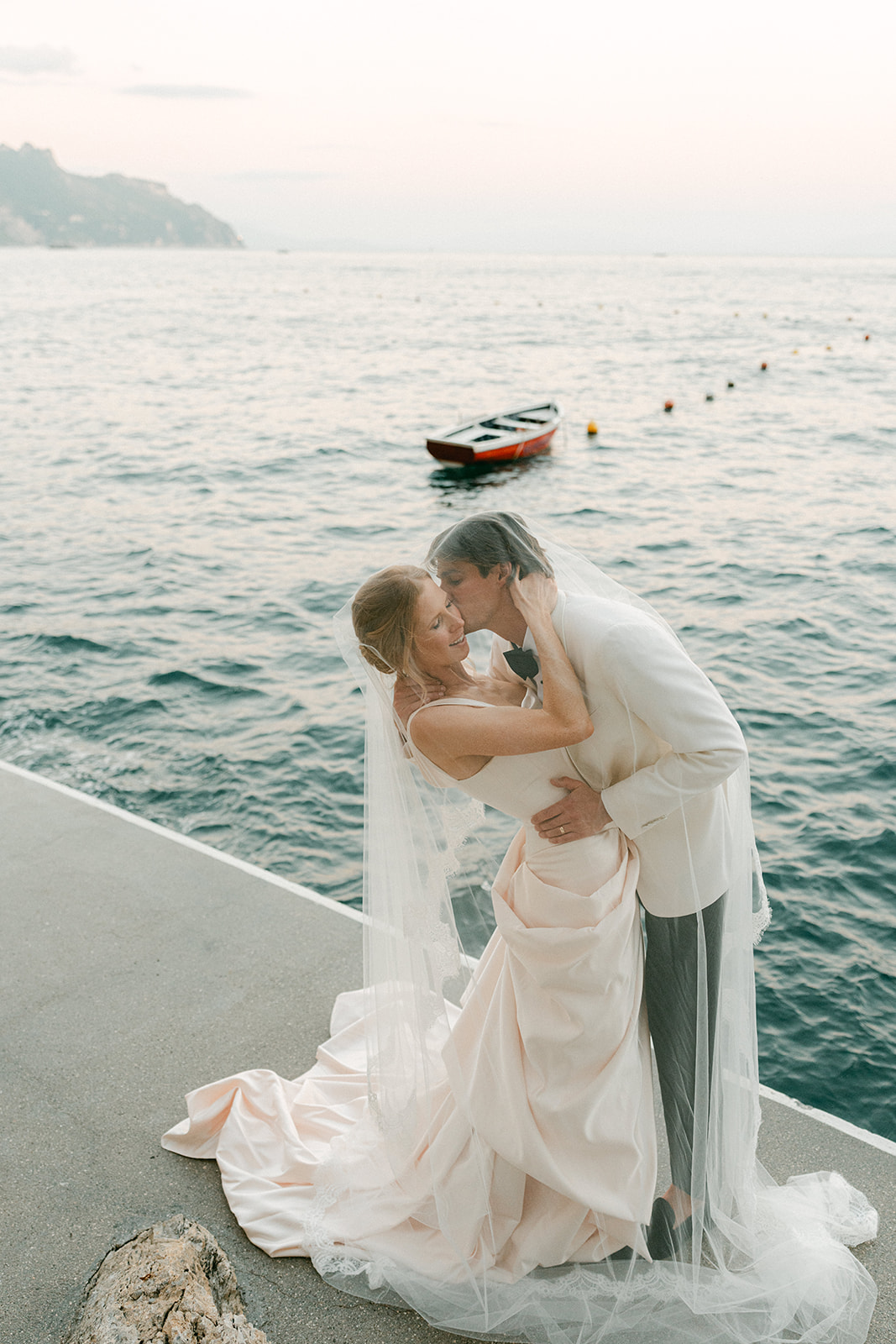 Elegant bride and groom posing on a luxury yacht in Italy after their Amalfi Coast wedding, surrounded by sparkling sea and cinematic coastal views.