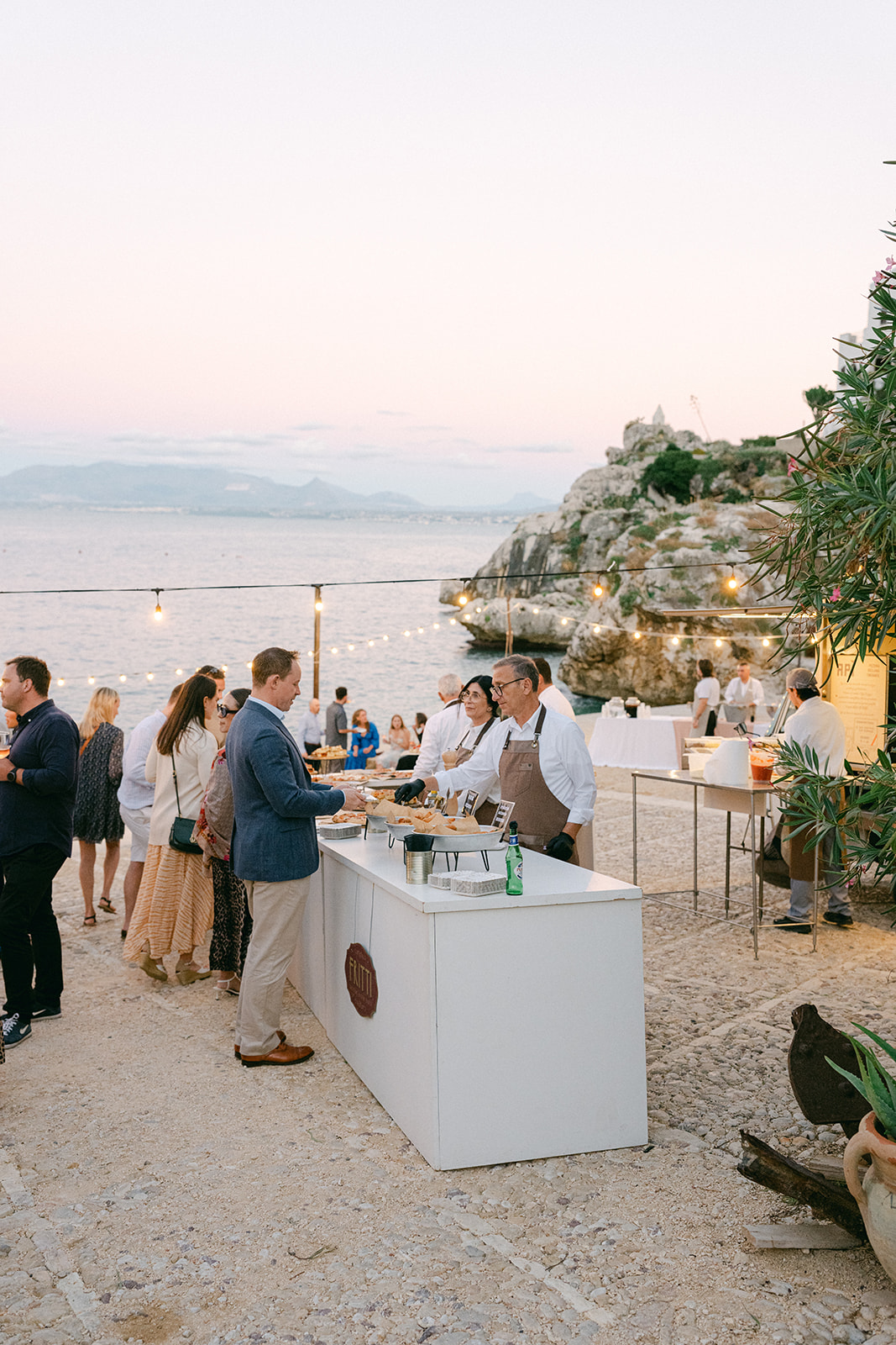 Guests enjoying Aperol spritz and fresh pizza at the day-one celebration for this Tonnara di Scopello wedding.