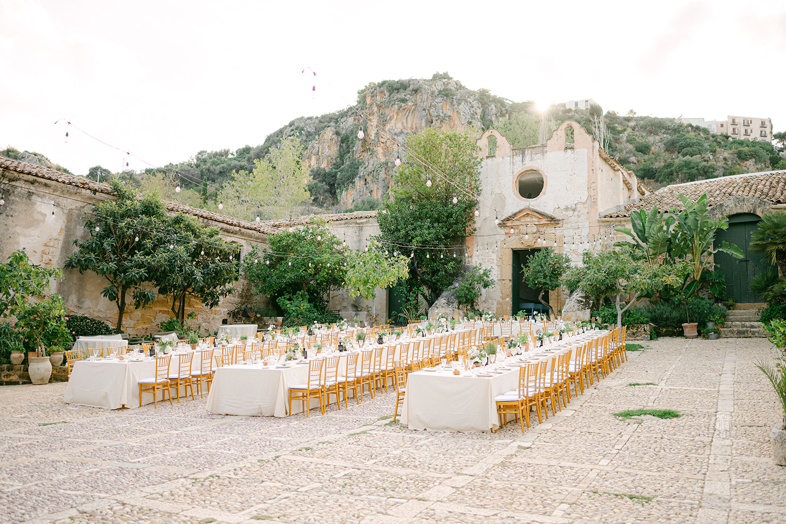 Long banquet tables in the rustic courtyard at Tonnara di Scopello set for Emma and Chris’s outdoor wedding reception in Sicily.